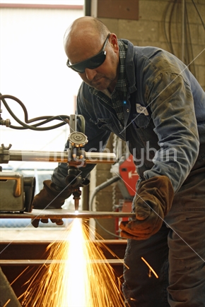 A tradesman in an engineering workshop, using a gas cutter to cut a metal plate 
