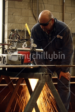 A tradesman keeping a close watch on a gas cutter cutting a metal plate in an engineering workshop.