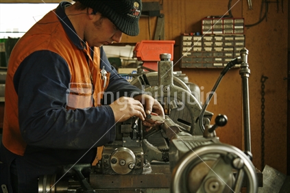 A young man  adjusting settings on a large industrial metal lathe, before commencing with tooling.