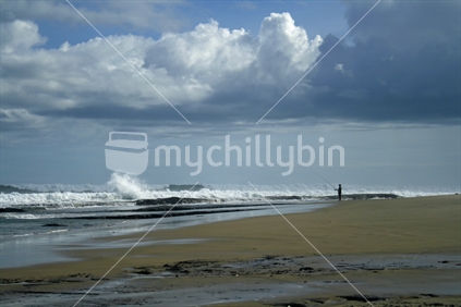 Waves crashing on a Northland beach, a man fishing in the distance.