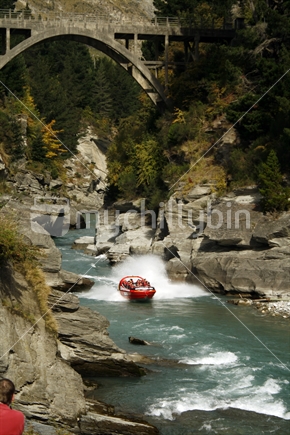 A jetboat racing down rock lined river rapids.  Central Otago.
