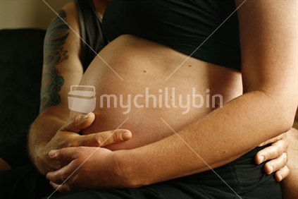 A father supporting a mother holding her unborn child in her belly.