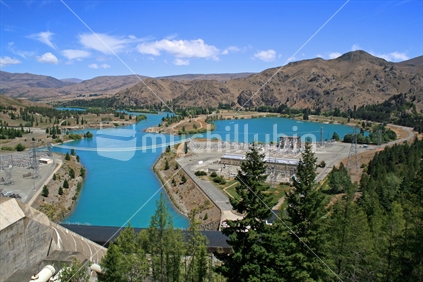 Looking from the roadway across the top of the largest man made dam in the southern hemisphere.  Benmore power station the beginning of Lake Aviemore and Sailors Inlet. New Zealand