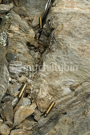 Spent bullet cartridges of a .22 rifle, fallen into rocky cracks.
