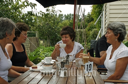 Four women chatting and laughing with each other, over a cup of coffee outdoors on a beautiful summers day.