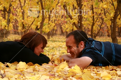 Making plans - a recently engaged mature couple lying on a carpet of golden autumn leaves, making plans for their wedding. 