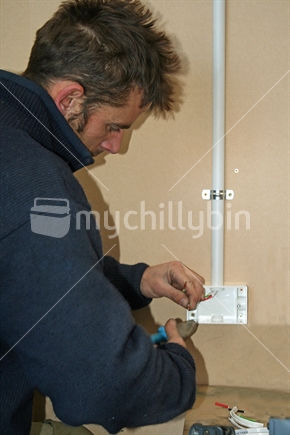 At work, an electrician installing wiring to a new electrical outlet.