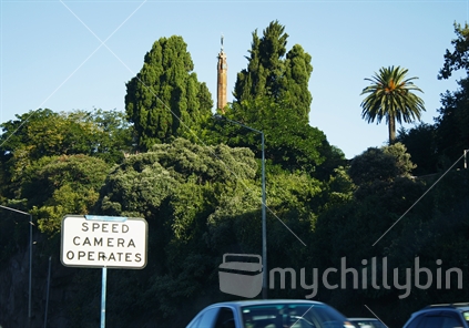 Speed camera sign on an Auckland Motorway, with monument in the distance.