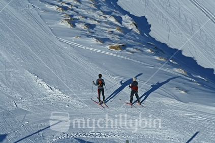 The distant figures of 2 skiers practicing on a groomed cross country ski surface in winter.