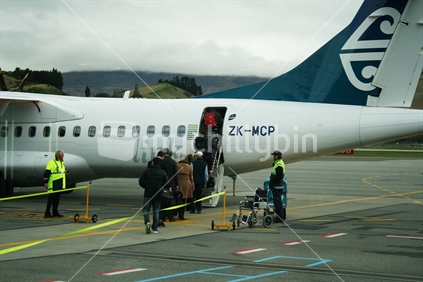 Passengers climbing the stairway onto an Air New Zealand link plane at Queenstown Airport.  Grab aq seat - Good for your wealth esteem sign.