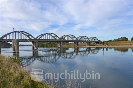 Iconic arches of Balclutha bridge, reflected in swift flowing, but calm Clutha River. Otago.