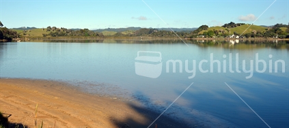 A calm estuary at Whananaki, with the longest footbridge in the southern hemisphere in the background.