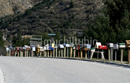 A line of rural post boxes of differing sizes shapes and colours.