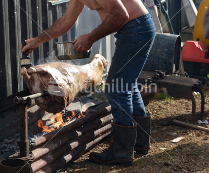 Although its winter solstice, basting a spit roasting lamb is hot work, an adult man has removed his shirt to cool down.