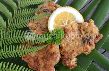 Crisp fresh, green lipped mussel fritters on woven flax mat with NZ fern and garnish. 