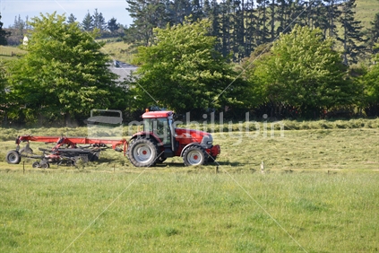 Farmer in his tractor tedding mown grass before bailing.