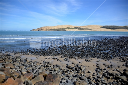 Ebbed tide exposing stone ground, with famous Opononi sandhills across Hokianga harbour, in the distance.