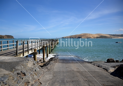 Calm waters of an ebbing tide, looking down the boatramp and along the wharf to the distant sandhills, at Omapere Beach.