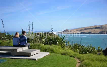 A young couple view Hokianga Harbour and the famous sandhills of Opononi from a carpark.