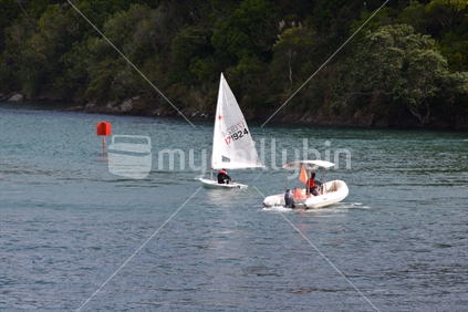 A support boat and teacher follow a learner yachtsman.