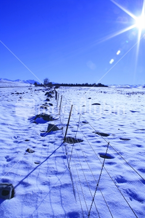 Snow covered pasture and partially buried barbed wire fence, South Island.