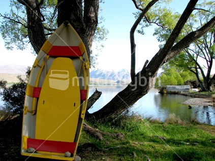 A yellow and red wooden dinghy leaning against a tree, lake edge.