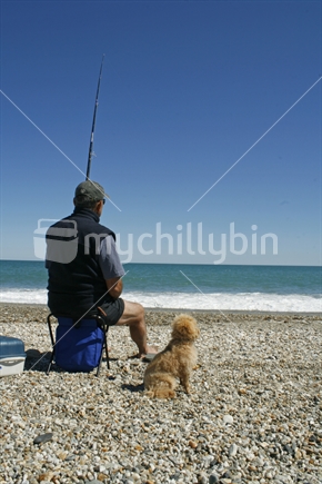 A man and his companion sitting, waiting for the fish to bite, on a West Coast beach, South Island.