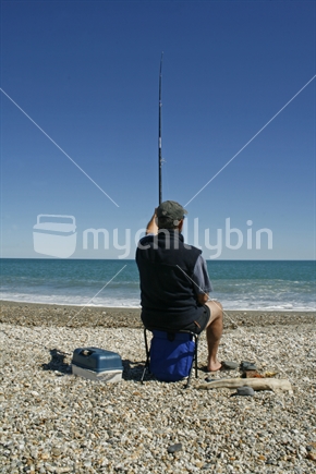 A man sitting, waiting for the fish to bite, on a West Coast beach, South Island.