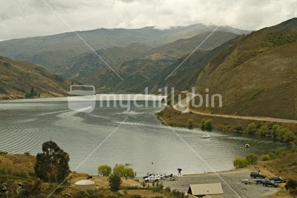 Vehicles and trailers parked by the boatramp, indicating that a grey stormy day didn't stop boaties from having fun on Lake Dunstan, Central Otago. Focus on near boats in water.