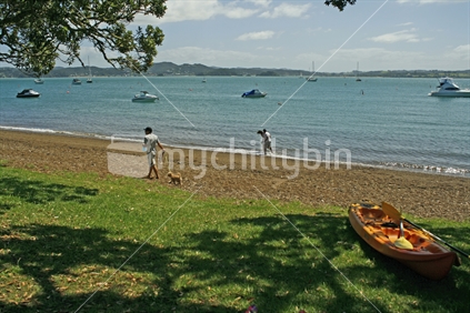 A man walking his dog while a couple enjoy the waters edge along Russell beach, Bay of Islands.