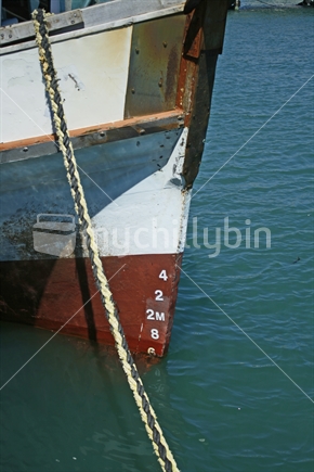 Bow of a boat docked at a wharf with plimsoll line and depth indicators, marks showing.