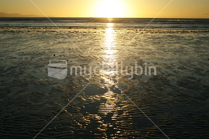 Setting sunlight reflected in the wet sand on the beach at ebb tide