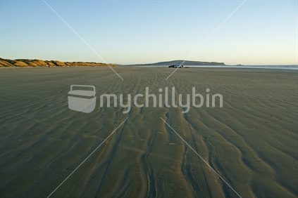 Tyre marks left by a vehicle blend in with natural tidal ripples in the sand.