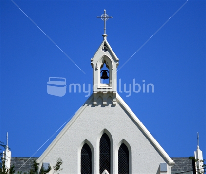 The cross and bell tower atop a church, clearly outlined with a clear blue sky background.