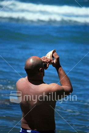 Man playing the putatara standing in the sea.