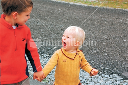 Two children holding hands, smiling and interacting while sharing a happy precious moment.