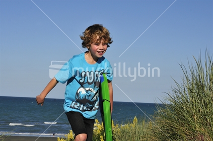 Boy with boogie board running over sand dunes at the beach.