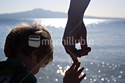 Son reaching to hold Father's hand, silhouetted against Rangitoto Island, Mission Bay, Auckland