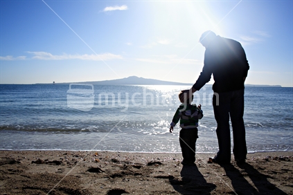 Father caring for son, silhouetted against Rangitoto Island, Mission Bay, Auckland