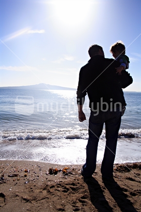 Father holding Son, silhouetted against Rangitoto Island, Mission Bay, Auckland
