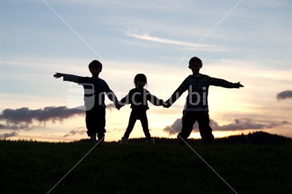 Three children holding hands, at sunset
