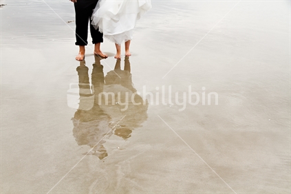 Wedding couples feet, and reflection on sand.