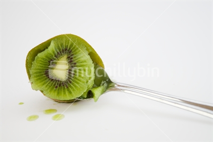 Tea spoon scooping kiwi fruit on a light grey background