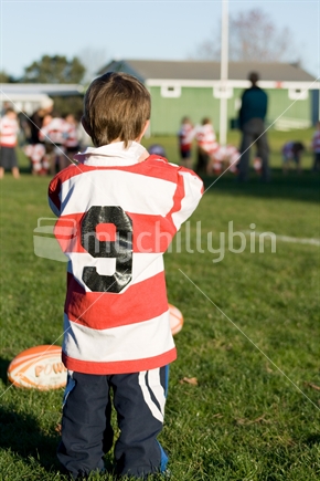 Little boy wearing rugby jersey watching little kids play rugby