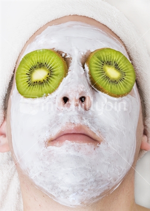 A relaxed man with face peel and kiwifruit in place of cucumber