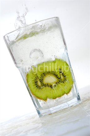 A slice of kiwifruit falling into a fizzy drink