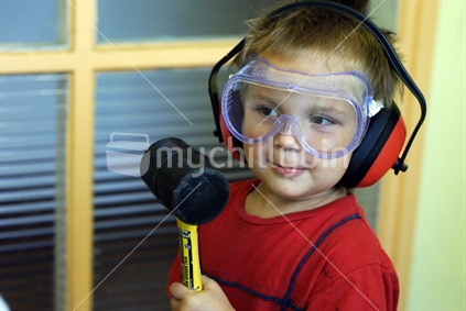 A boy wearing safety gear holding a rubber mallet