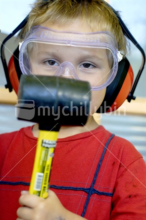 A boy wearing safety gear holding a rubber mallet