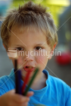 A boy holds coloured pencils
