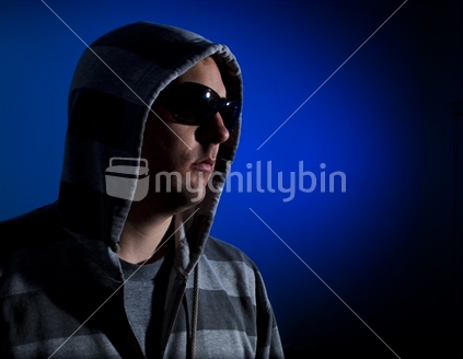 A male with serious pose wears a hoodie in a blue setting